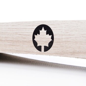 Nahaufnahme einer hellen Holzoberfläche mit einem schwarzen, runden Logo eines Ahornblattes, vor einem glatten, sauberen Hintergrund.