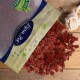 Eine Tüte "Pure Pet" Leckerlis, die rote würfelförmige Stücke auf eine Holzoberfläche fallen lässt, beschriftet mit "100% Natürlich" und "Premium Qualität."