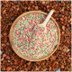 Bunte Haustierfutterpellets in einer Holzschüssel mit einem Schaufel, vor einem strukturierten rötlich-braunen Hintergrund.