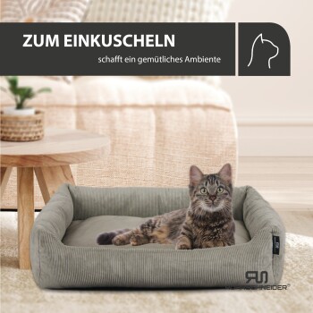 Eine getigerte Katze liegt in einem gemütlichen Bett in einem warmen Wohnzimmer mit einem Holztisch. Text: "ZUM EINKUSCHELN schafft ein gemütliches Ambiente."