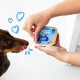 Une personne tient un contenant de nourriture pour chien Edgard Cooper étiqueté 'Yummy Salmon & Turkey' tandis qu'un chien brun lèche avidement ses lèvres.