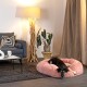 Ein schwarz-brauner Hund ruht auf einem flauschigen rosa Haustierbett in einem gemütlichen Wohnzimmer mit einem grauen Sofa, einer dekorativen Lampe und Topfpflanzen.