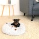 Ein kleiner schwarz-brauner Hund ruht sich in einem flauschigen grauen Haustierbett auf einem hellen Teppich aus, mit einem modernen grauen Sofa und einem Beistelltisch im Hintergrund.