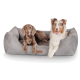 Zwei Hunde, die auf einem plüschigen grauen Hundebett entspannen, einer mit braunem Fell und der andere mit weißem und braunem Fell, beide sehen entspannt aus.