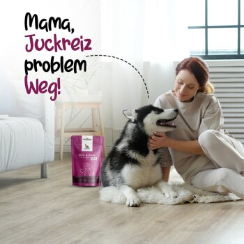 Eine Frau lächelt, während sie einen schwarz-weißen Hund auf dem Boden streichelt, neben einer pinken 'Skin & Foot'-Tasche mit verspieltem Text.