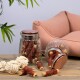 Ein Glasbehälter mit Hundeleckerlis und ein umgekipptes Glas stehen auf einem Holztisch neben einem plüschigen rosa Hundebett und einem Seilspielzeug.