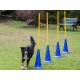 Ein schwarzer und brauner Hund läuft an vier blauen Agility-Kegeln mit gelben Stangen in einem grasbewachsenen Garten vorbei und zeigt ein Trainingssetup.