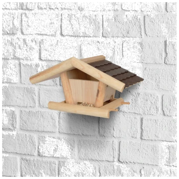 Wooden birdhouse with a sloped roof, mounted on a white brick wall, featuring a small feeding area at the base.