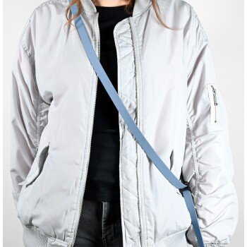 Eine Person trägt eine hellgraue Bomberjacke über einem schwarzen Shirt, mit einem sichtbaren blauen Umhängegurt.