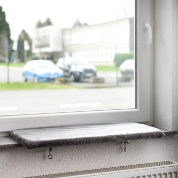 Eine graue Katzenfensterliege, die auf einer Fensterbank montiert ist, mit Blick auf geparkte Autos und ein Gebäude draußen.