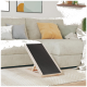 Eine hölzerne Haustierrampe mit einer schwarzen Oberfläche steht vor einem hellen Sofa, das mit bunten Kissen geschmückt ist, in einem gemütlichen Wohnzimmer.