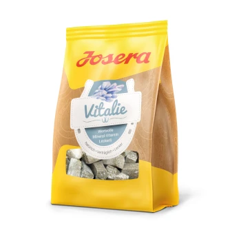 Ein gelber Beutel Josera Vitalie, gekennzeichnet als wertvoller Mineral-Vitamin-Leckerbissen für Haustiere, mit kleinen, glänzenden, quadratischen Leckerlis darin.