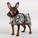 Ein kleiner Hund trägt einen stylischen grauen Regenmantel mit Camouflage-Muster, Kapuze und verstellbaren Riemen, steht vor einem hellen Hintergrund.