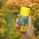 Eine Hand hält einen gelben Behälter mit JBL Pro Novo Spirulina Fischfutterflocken, beschriftet mit "Herbivore" und "Flakes M", mit einem verschwommenen aquatischen Hintergrund.