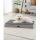 Ein kleiner weißer Hund ruht auf einem grauen Haustierbett mit plüschiger Oberseite, das auf einem weichen, hellen Teppich in einem modernen Wohnzimmer platziert ist.