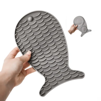 Eine Person hält eine graue Silikon-Futtermatte für Haustiere in Fischform, ausgestattet mit strukturierten Schuppen für besseren Halt.