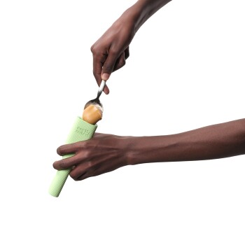 Une personne prenant du beurre de cacahuète d'un moule à friandises pour animaux en silicone vert avec une cuillère en métal, montrant les mains et la texture du moule.