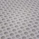 Eine Nahaufnahme einer strukturierten weißen Oberfläche mit zahlreichen gleichmäßig verteilten runden Löchern, die einem perforierten Design ähneln.
