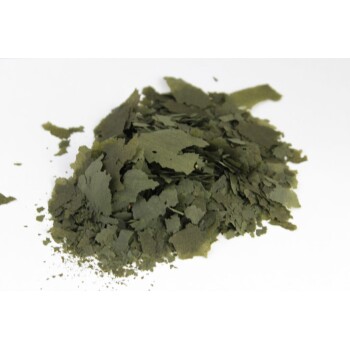 Ein Haufen grüner, blättriger Flocken, die getrocknetem Algen oder Spirulina ähneln, vor einem weißen Hintergrund.
