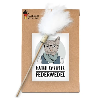 Ein braunes Paket mit einer Cartoon-Katze in Brille und Schal, beschriftet mit "KATER KASIMIR FEDERWEDEL" und markiert mit "HANDMADE WITH LOVE", mit einem Feder-Spielzeug.