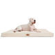 Ein großer weißer Hund entspannt sich auf einem cremefarbenen Tierbett mit einem Holzschild, das Komfort und Stil zeigt.