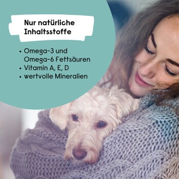 Ein kleiner weißer Hund kuschelt im Schoß, eingewickelt in eine Decke. Der Text erwähnt Omega-3, Omega-6, Vitamine A, E, D und Mineralien.