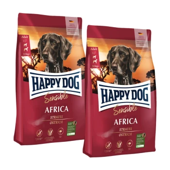 Zwei Säcke Happy Dog Sensible Africa Erwachsenen-Hundefutter mit Strauß, mit schwarzem Hund und Sonnenuntergang im Hintergrund.