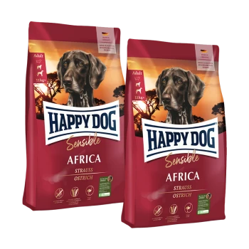 Zwei Säcke Happy Dog Sensible Africa Erwachsenen-Hundefutter mit Strauß, mit schwarzem Hund und Sonnenuntergang im Hintergrund.