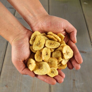 Hände halten einen Stapel getrockneter Bananenchips über einer Holzoberfläche, Haustiersnack aus einem Onlineshop.