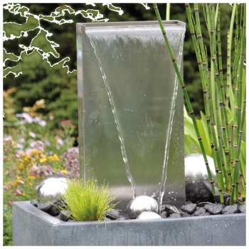 Ein moderner Wasserbrunnen mit einer eleganten, transparenten Platte, aus der Wasser herabfließt, umgeben von dekorativen silbernen Kugeln und grünen Pflanzen.