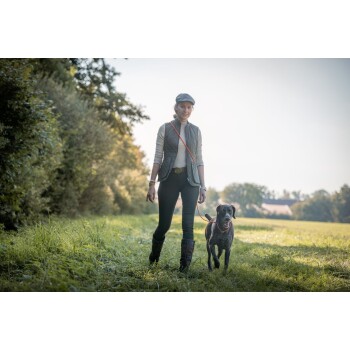 Frau führt einen schwarz-weißen Hund an roter Leine über ein sonniges Grasfeld