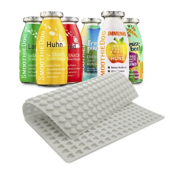 Bunte Smoothieflaschen für Hunde, beschriftet mit Geschmacksrichtungen wie "Huhn" und "Rind", neben einer rosa Silikonmatte mit Herzformen.