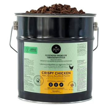 Ein schwarzer Metallbehälter mit Trockenfutter für Hunde, beschriftet mit 'Crispy Chicken' und natürlichen Zutaten: Huhn, Banane, Kartoffeln, Thymian.