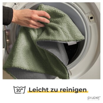 Eine Hand, die eine weiche, grüne Haustierdecke in eine Waschmaschine legt, mit dem Text 'Leicht zu reinigen' darunter.