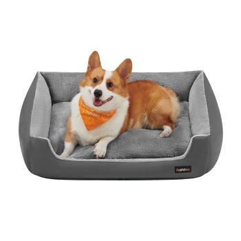 Ein glücklicher Corgi mit einem leuchtend orangefarbenen Halstuch ruht auf einem plüschigen grauen Hundebett und zeigt Komfort und Stil.