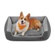 Ein glücklicher Corgi mit einem leuchtend orangefarbenen Halstuch ruht auf einem plüschigen grauen Hundebett und zeigt Komfort und Stil.