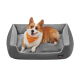 Ein glücklicher Corgi mit einem leuchtend orangefarbenen Halstuch ruht auf einem plüschigen grauen Hundebett und zeigt Komfort und Stil.
