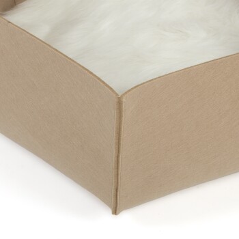 Nahaufnahme eines Haustierbettes mit einem weichen, weißen Fellinneren und einem beigen Stoffäußeren, das die abgerundeten Ecken und Nähte zeigt.