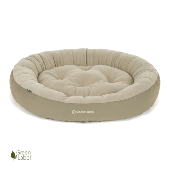 Rundes, plüschiges Hundebett in hellem Beige mit gestepptem Design, mit dem Logo 'Doctor Bark' und einem 'Green Label'-Symbol.