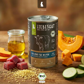 Dose Liebesgut Hundefutter mit Aufschrift 'Bio‑Rind für Welpen', umgeben von Rindfleischwürfeln, Hirse, einem Glas Öl, Kürbis und Zucchini.