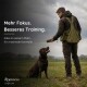 Person in orangefarbener Jacke hält Ball, trainiert sitzenden Golden Retriever auf grasigem Weg in ländlichem Feld.