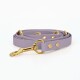 Eine lavendelfarbene Haustierleine mit goldenen Beschlägen und dekorativen Nieten, ordentlich auf einem weißen Hintergrund aufgerollt.