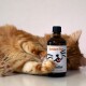 Eine verspielte orange Katze liegt neben einer Flasche mit der Aufschrift "Better Fur", mit einem Cartoon-Katzenkopf und dem Text "Made in Germany."