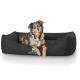 Ein braun-weißer Hund liegt auf einem schwarzen Hundebett, mit dem Logo "KNUFFELWELT" sichtbar auf der Vorderseite.