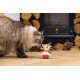 Fluffy cat sniffing a small reindeer plush toy with a red base on a wooden floor near stacked firewood.
