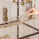 Eine Hand entfernt ein Schiebepanel aus einem Vogelkäfig, der bunte Spielzeuge und Sitzstangen enthält.