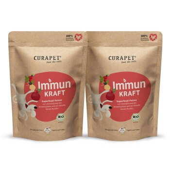 Zwei Beutel CURAPET Immun Kraft Superfood-Pulver für Hunde, mit einer verspielten Hundillustration und Text auf Deutsch über die Unterstützung des Immunsystems.