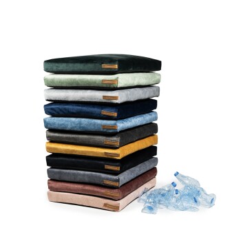 Ein Stapel bunter Haustierkissen in Grün, Grau, Blau, Schwarz, Gelb und Pink, neben weggeworfenen Plastikflaschen.