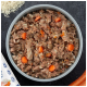 Bol de nourriture humide pour chien avec riz et morceaux de carotte, grains de riz et une carotte sur une surface sombre.