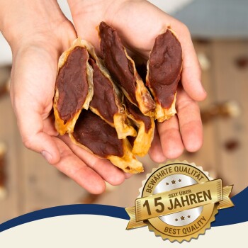 Eine Person hält mehrere Stücke Haustierleckerlis, die ihre kaubare Textur zeigen. Ein Abzeichen liest "Beste Qualität" und "15 Jahre" auf Deutsch.